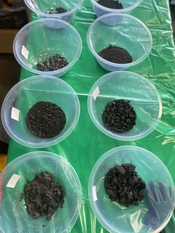 Small clear sample tubs holding separate portions of dark material on a workbench.