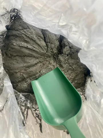 A green scoop in a bag of grey sample material.